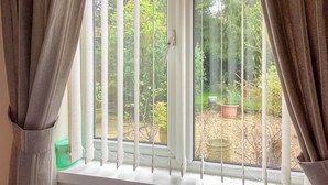 A window with white blinds and brown curtains, offering a view of a garden with potted plants and a small outdoor area.