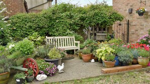 A garden with a bench, various potted plants, a bird statue, and a brick wall.