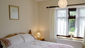 Et soveværelse med seng, et natbord, en lampe, et vindue med gardiner og et billede hængt på væggen.