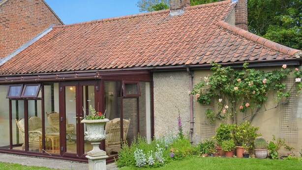 Et traditionelt hus med et tegltag, et orangeri med glasdøre og en have med plantekasser og et fuglebad.