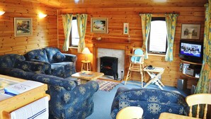 Un intérieur de chalet chaleureux avec une cheminée, des murs en bois et des meubles à motifs bleus.