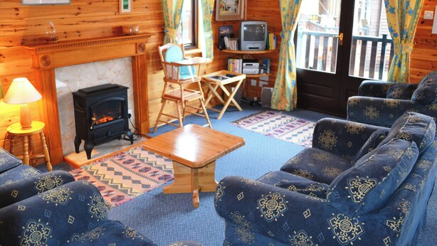 L’intérieur chaleureux d’un chalet avec une cheminée, des meubles en bois, un téléviseur et une vue sur la terrasse extérieure.