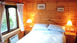 Une chambre à coucher dans un chalet en bois, avec un lit, deux lampes de chevet, une fenêtre avec des rideaux et deux tableaux encadrés accrochés au mur.