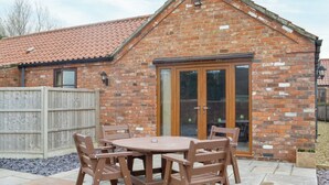 A brick house with a tiled roof, a wooden fence, and a patio with a round table and chairs. - George's Gaff - E4432 (Near Skegness)
