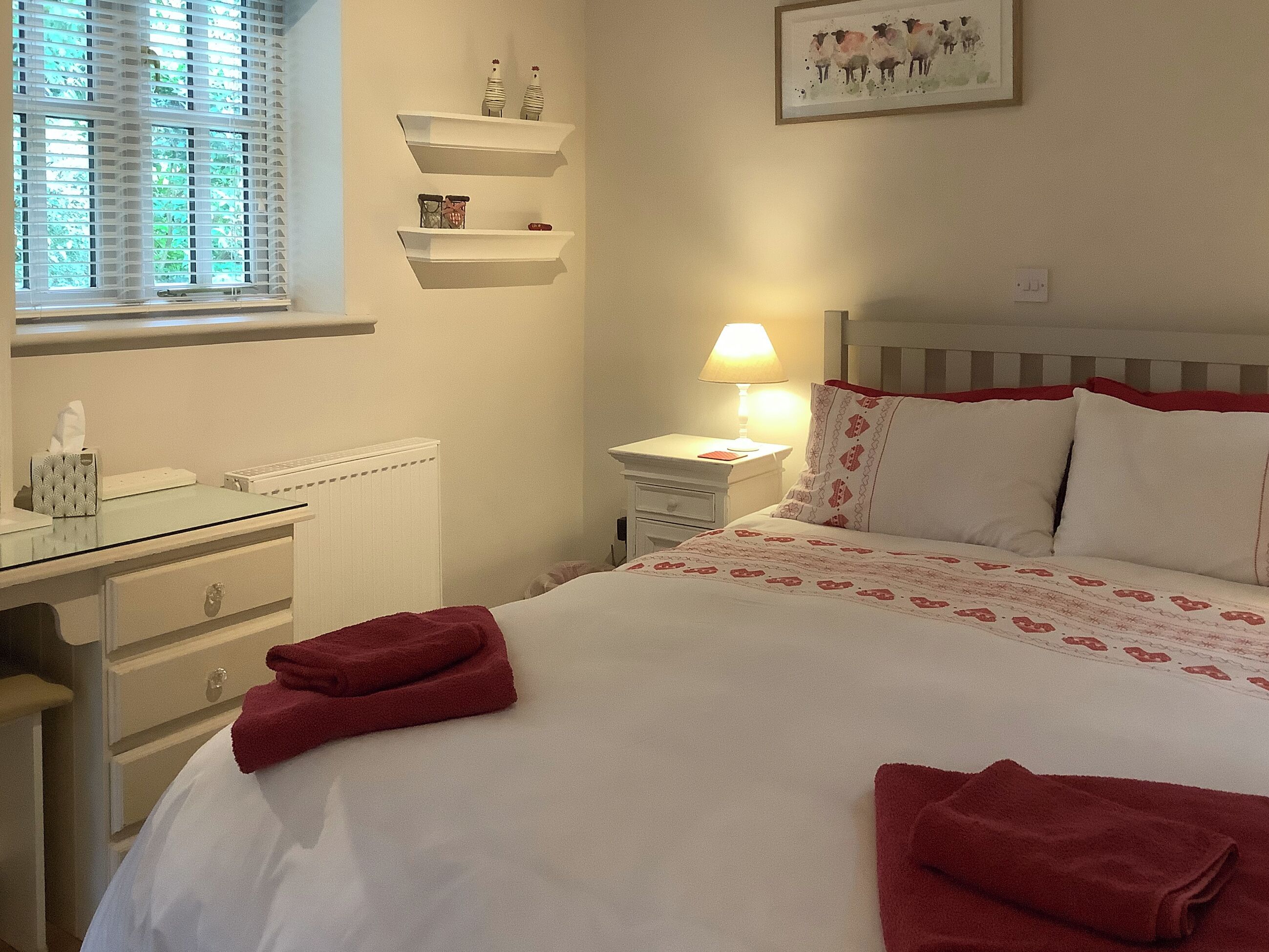 A neatly arranged bedroom with a bed, bedside table, lamp, and a window with blinds.