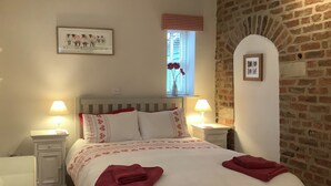 Ein ordentlich bezogenes Bett mit einer rot-weißen Tagesdecke, zwei rote Handtücher und zwei Nachttische mit Lampen.