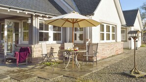 Une maison dotée d’un patio comprenant une table, des chaises et un parasol.
