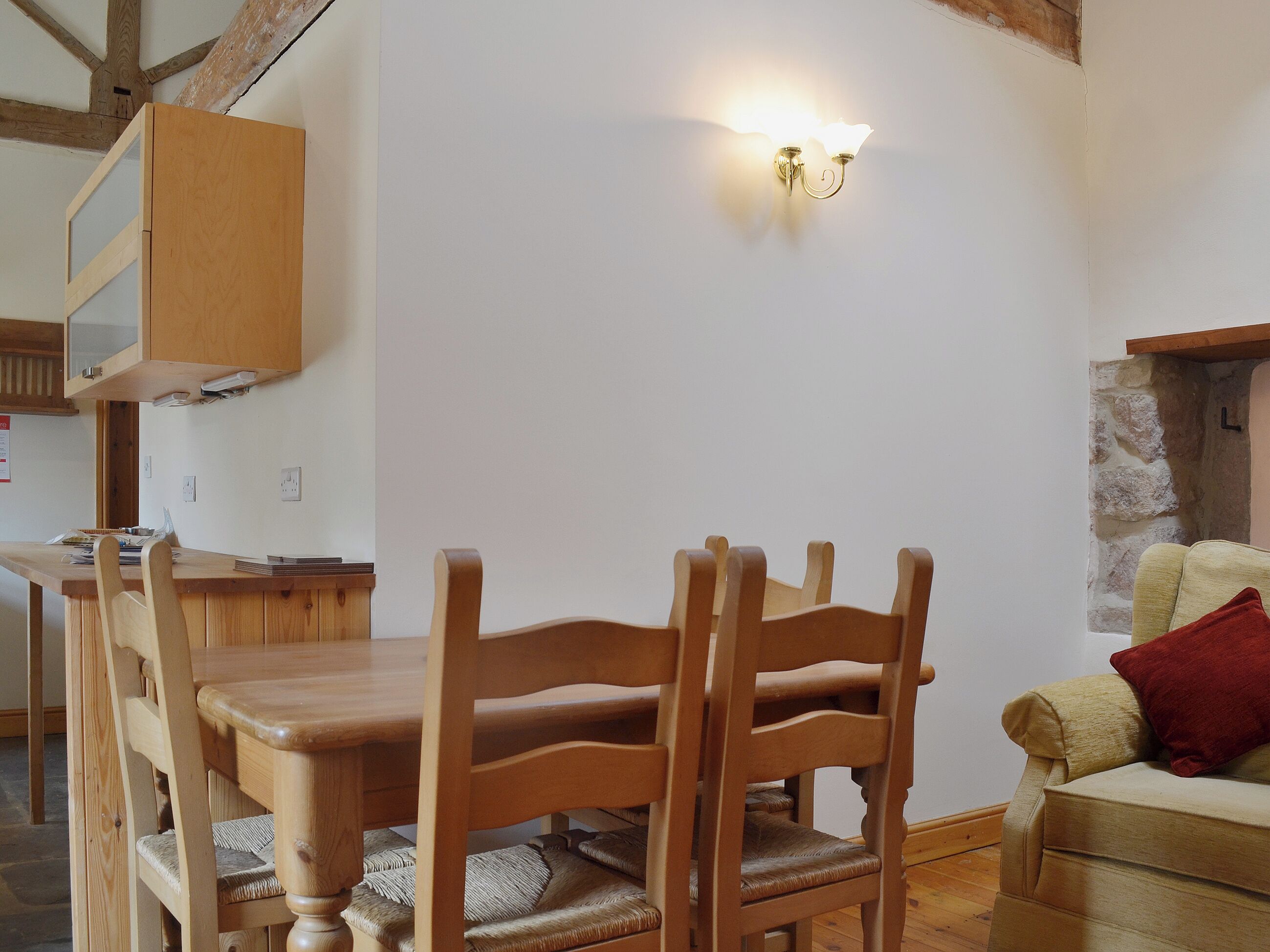 Een eetgedeelte met houten stoelen en een tafel, een wandlamp en een stenen muur op de achtergrond.