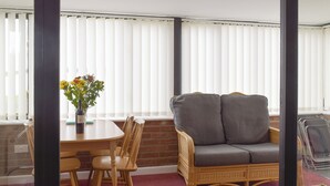 A room with a dining table, chairs, a wicker sofa, and a window with vertical blinds. - Carol's Cottage - E3043 (Wenhaston, near Southwold)