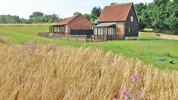 A rural barn with a red roof and a smaller adjacent structure, surrounded by a fenced field and trees in the background. - Carol's Cottage - E3043 (Wenhaston, near Southwold)