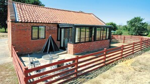 A brick building with a tiled roof, large windows, and a fenced outdoor area with tables and chairs. - Carol's Cottage - E3043 (Wenhaston, near Southwold)