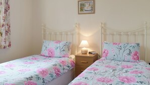 A bedroom with two single beds, each with floral bedding, a bedside table with a lamp, and a framed picture on the wall. - Carol's Cottage - E3043 (Wenhaston, near Southwold)
