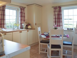 Una cocina con una mesa de comedor para dos personas, una ventana con cortinas y vistas al exterior.