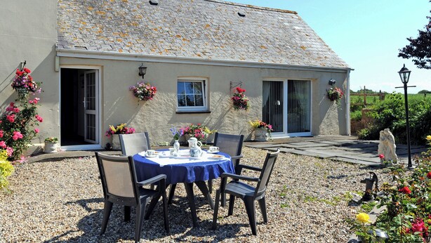 A building with a stone roof, a gravel patio, and a table set for two with chairs. - 2 bedroom accommodation in Cosheston near Pembroke (Cosheston near Pembroke)