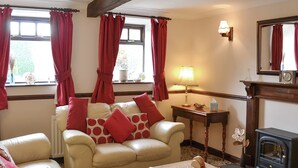 Un salon avec un canapé beige, des coussins rouges, une table basse en bois, une cheminée et une fenêtre ornée de rideaux rouges.