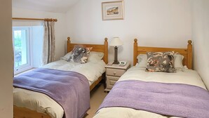 Ein Schlafzimmer mit zwei Betten, einem Nachttisch mit Lampe, einem Fenster mit Vorhängen und einem gerahmten Bild an der Wand.