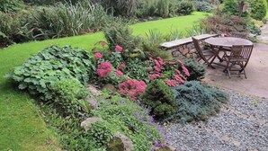 Ein Garten mit Steinmauer, Holztisch und Stühlen sowie verschiedenen Pflanzen.