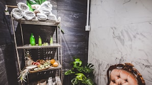 A bathroom with a marble wall, a shelf with towels, bottles, and fruits, and a plush chair. - Wherever Boutique Hostel (Rovaniemi)