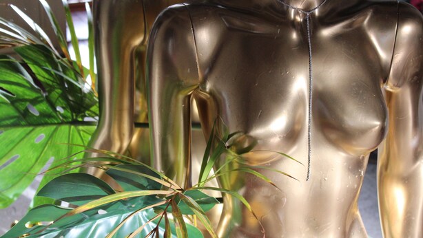 A golden mannequin torso with a zipper detail, surrounded by green foliage. - Wherever Boutique Hostel (Rovaniemi)