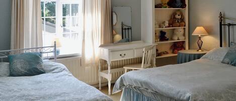 A bedroom with two beds, a dresser, a desk, and a window with curtains.