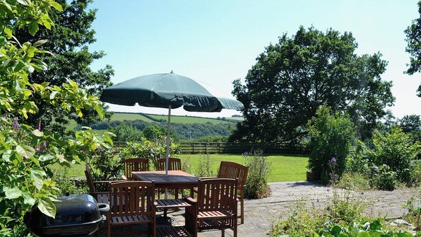 Une terrasse extérieure avec une table et des chaises, un barbecue et un parasol.