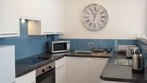 A modern kitchen with white cabinets, a microwave, a kettle, and a wall clock. - 2 bedroom accommodation in St Austell (St Austell)