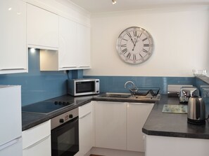 Una cocina moderna con armarios blancos, un microondas, un hervidor y un reloj de pared.