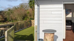 A wooden deck with a railing, a small round table, and a door leading to an interior space. - 2 bedroom accommodation in St Austell (St Austell)