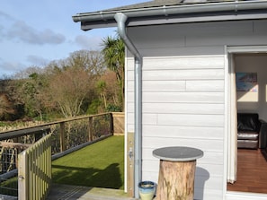 A wooden deck with a railing, a small round table, and a door leading to an interior space. - 2 bedroom accommodation in St Austell (St Austell)