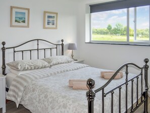 Una cama bien hecha con cabecera, una mesita de noche con lámpara y dos cuadros enmarcados en la pared.