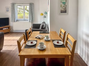 Un comedor con una mesa dispuesta para dos personas, un sofá, un televisor y una ventana con cortinas.