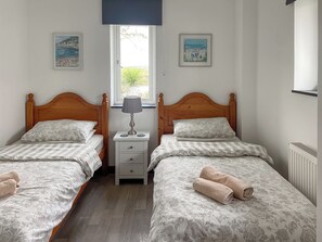 Una habitación con dos camas, una mesita de noche, una lámpara y dos cuadros en las paredes.