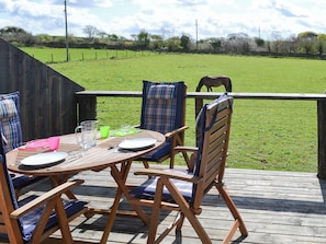 Una terraza de madera con una mesa dispuesta para cuatro personas, rodeada de sillas con cojines azules.