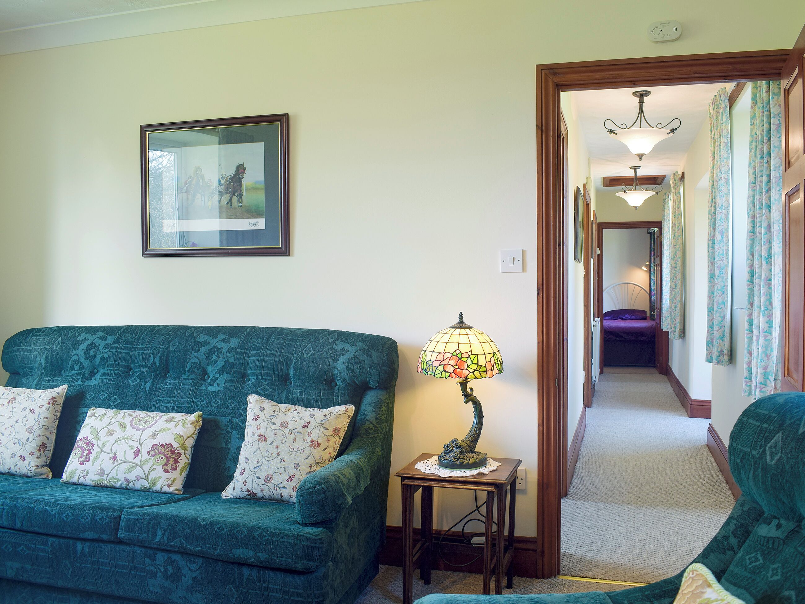 A living room with a sofa, a lamp, a framed picture, and a hallway leading to another room.