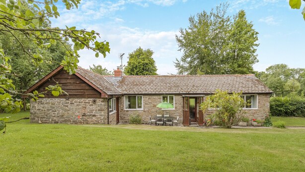Une petite maison en pierre avec un toit en tuiles, un porche en bois et un petit jardin.
