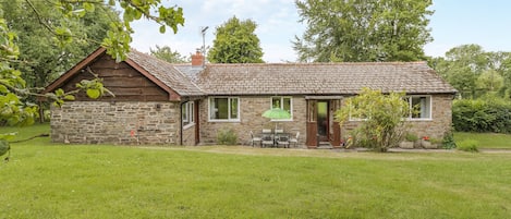 Une petite maison en pierre avec un toit en tuiles, un porche en bois et un petit jardin.