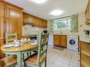A kitchen with wooden cabinets, a dining table set with plates and cups, a washing machine, and a window with curtains.