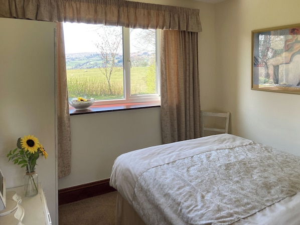 A bedroom with a bed, a window with curtains, a vase with flowers, and a painting on the wall.