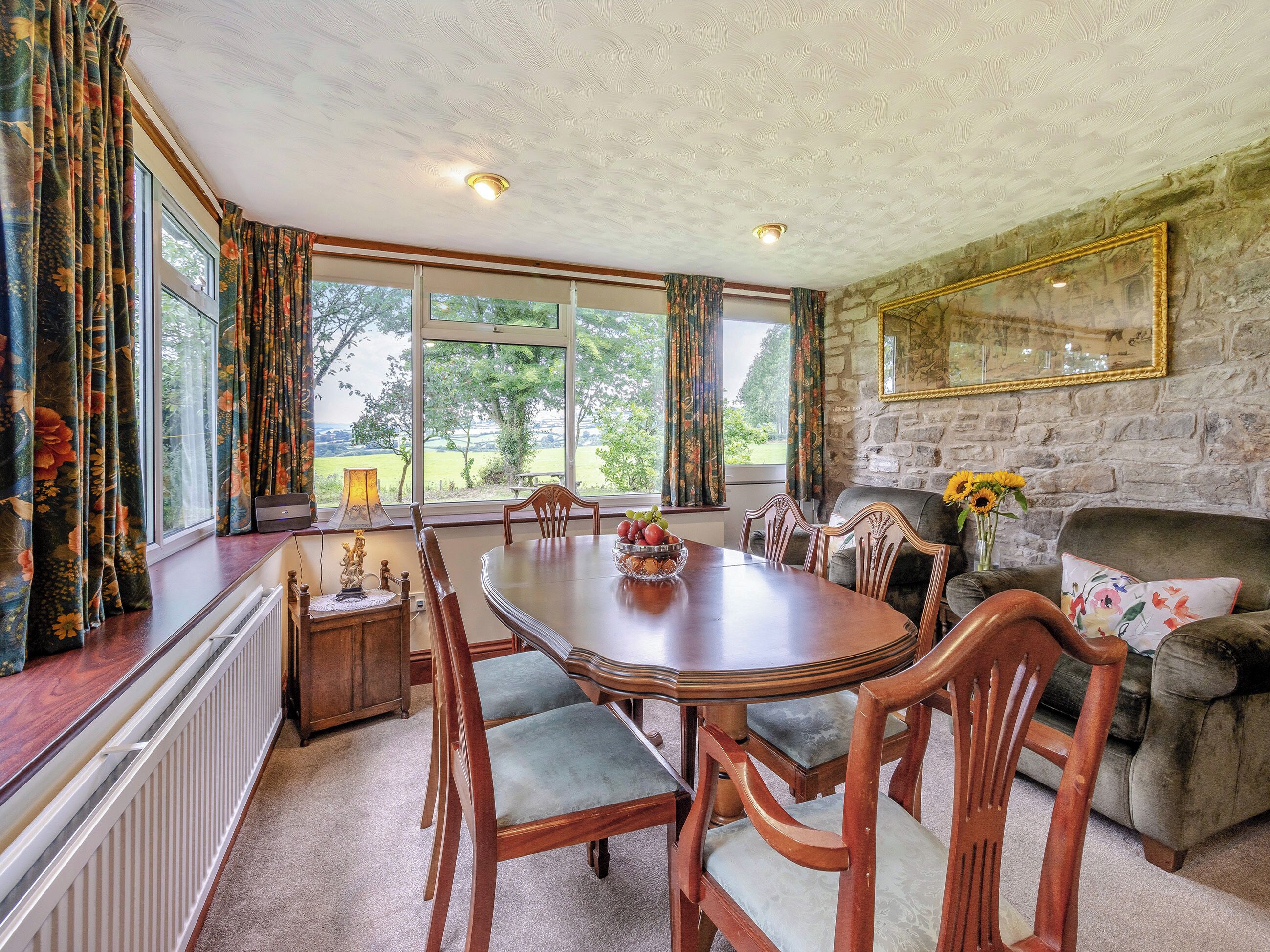 A dining area with a large table, chairs, a fireplace, and a stone wall.