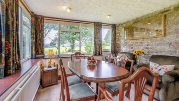 A dining area with a large table, chairs, a fireplace, and a stone wall.