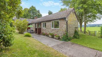 A stone cottage with a garden, a patio with a table and chairs, and a view of the countryside.