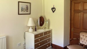 Une chambre à coucher avec un lit, une commode, un miroir, une chaise et une porte.