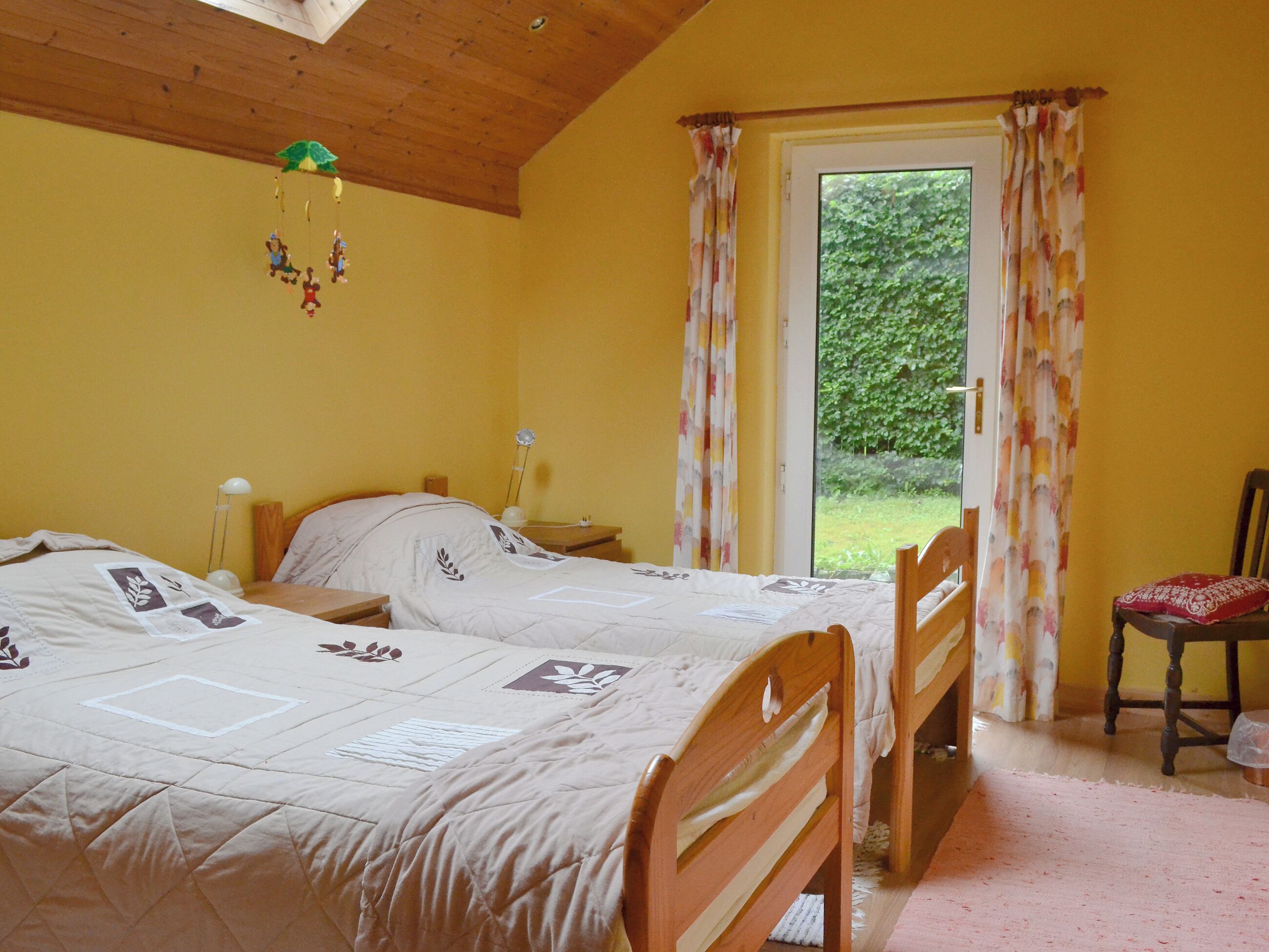 A bedroom with two beds, a wooden ceiling, a nightstand with a lamp, and a chair.