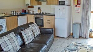 Et kompakt køkken med træskabe, en mikrobølgeovn, et køleskab, en vaskemaskine og et spiseområde med en sofa og en måtte.