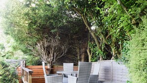 Une terrasse en bois avec des meubles en osier et un mur en briques.