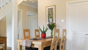 Un coin repas avec une table en bois, des chaises, un vase rouge orné de fleurs et un tableau encadré accroché au mur.