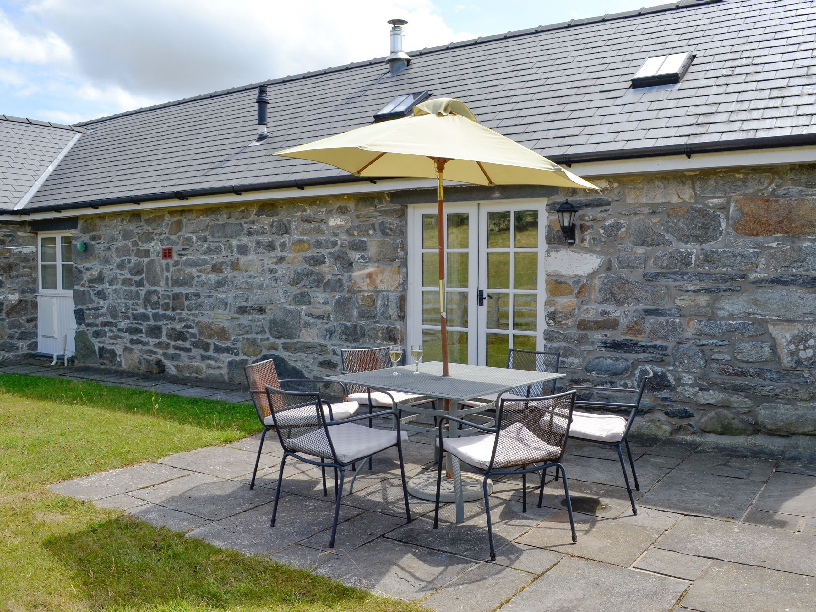 A stone building with a patio area featuring a table and chairs, a glass door, and a stone wall.