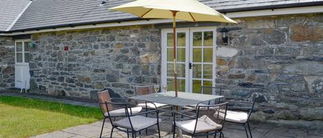 A stone building with a patio area featuring a table and chairs, a glass door, and a stone wall.