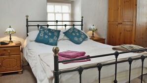 Um quarto com uma cama, duas mesas de cabeceira, um guarda-roupa de madeira e uma janela.