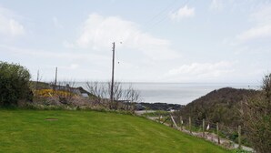 Paisagem costeira com um campo gramado, uma cerca de madeira e vista para o mar.